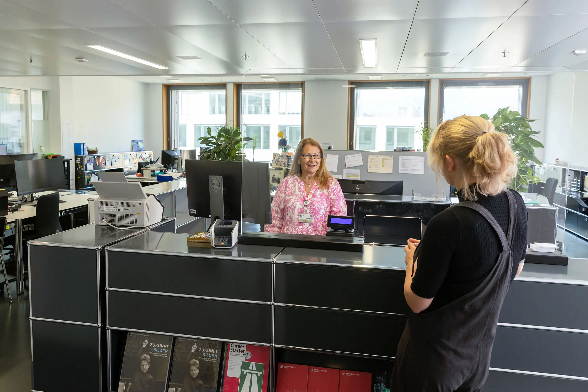 Eine Frau wird am Schalter der Kanzlei von einer Mitarbeiterin empfangen.