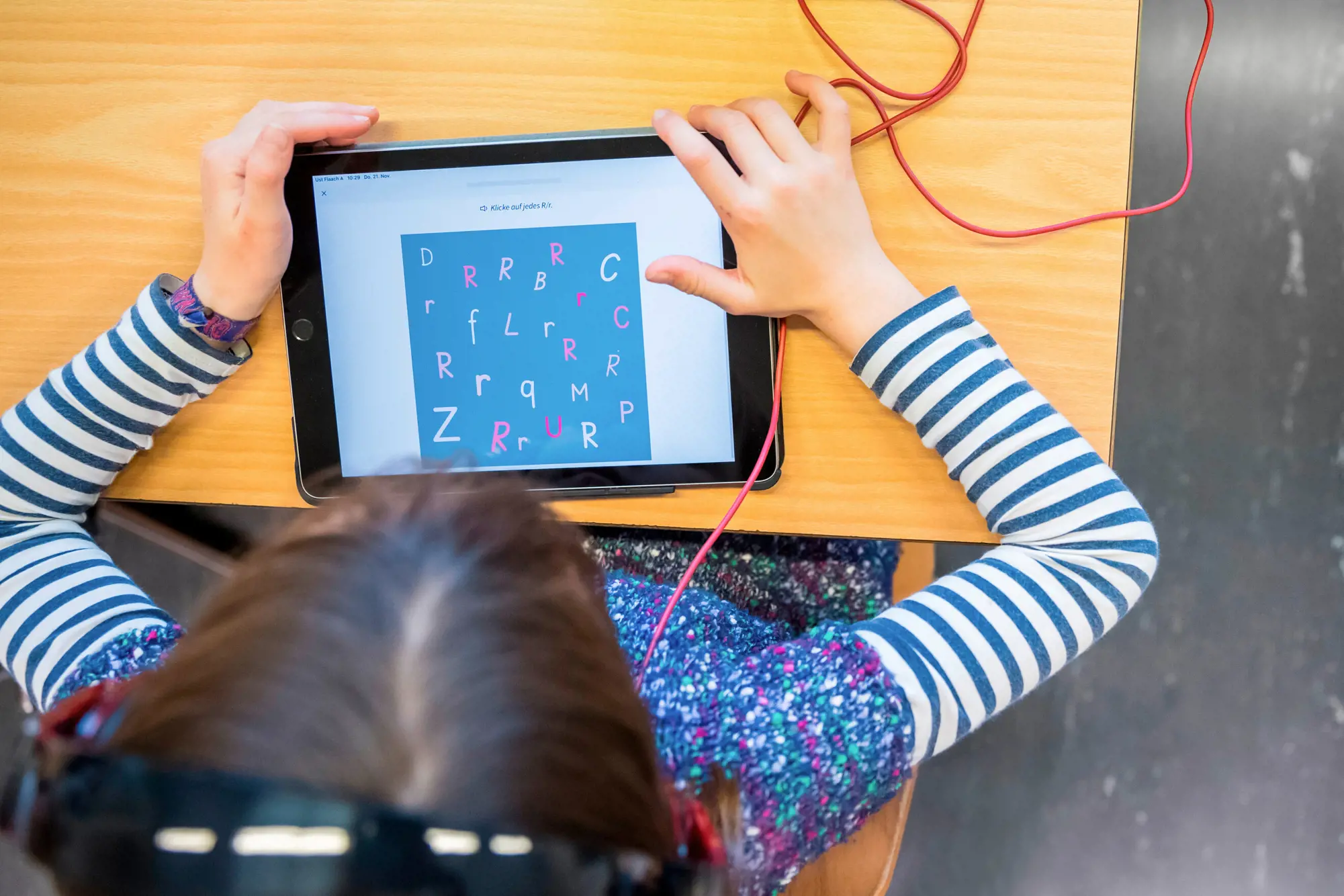 Ein Kind (aufgenommen von oben) löst in einem Tablet eine Aufgabe.